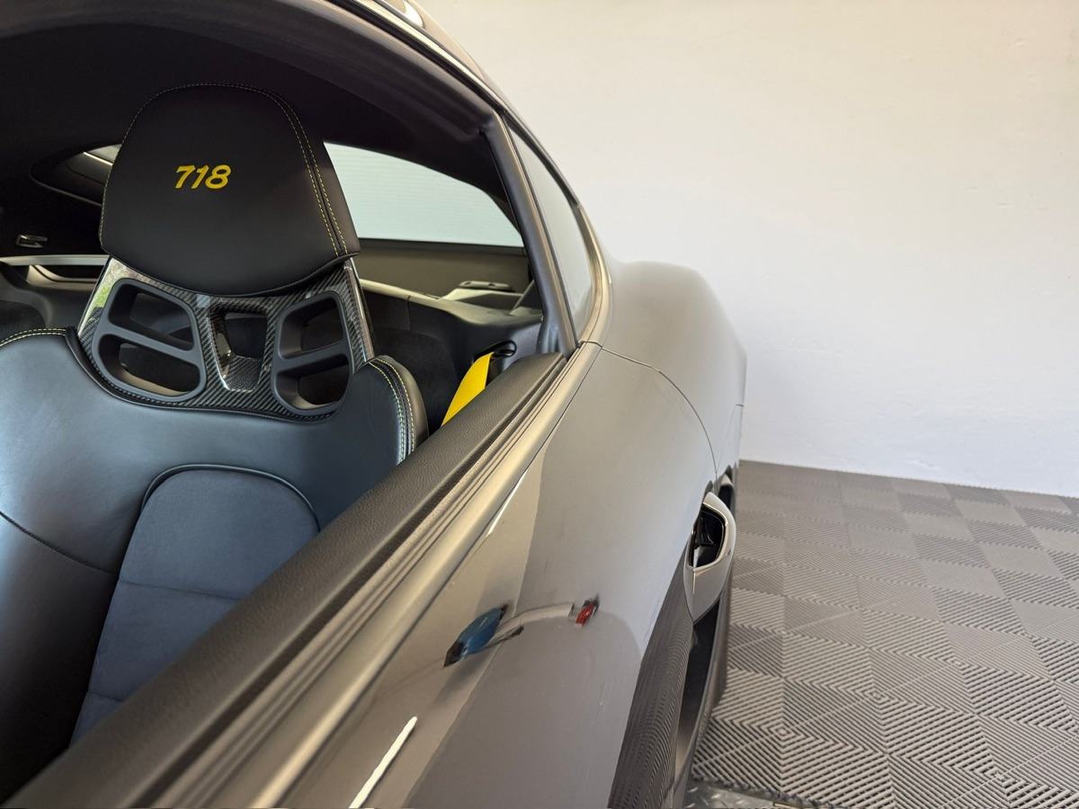 Grauer Porsche Sportwagen mit schwarzem Ledersitz und gelber "718"-Stickerei.