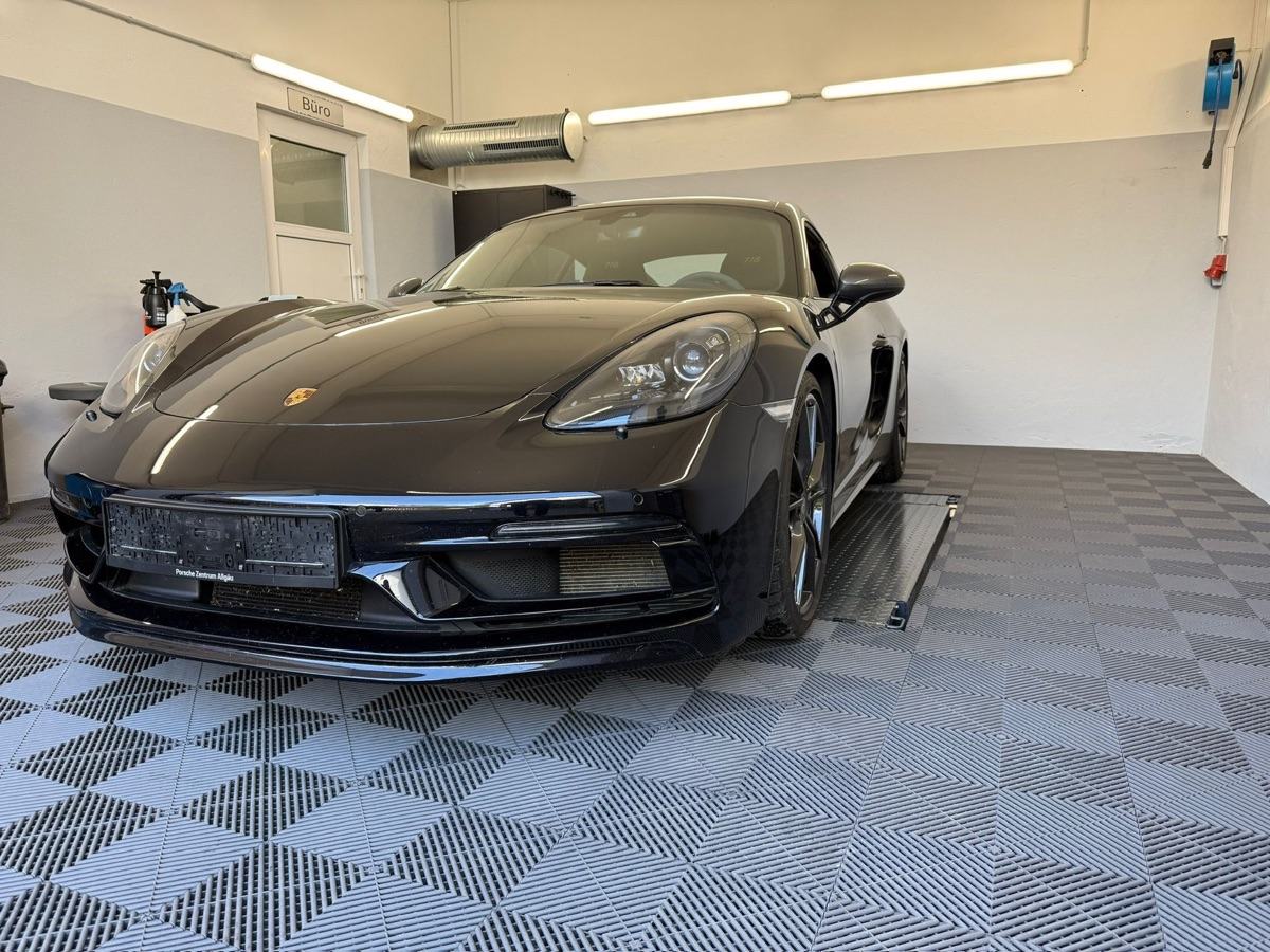 Schwarzer Porsche Sportwagen parkt auf einem grauen Fliesenboden in einer Garage.
