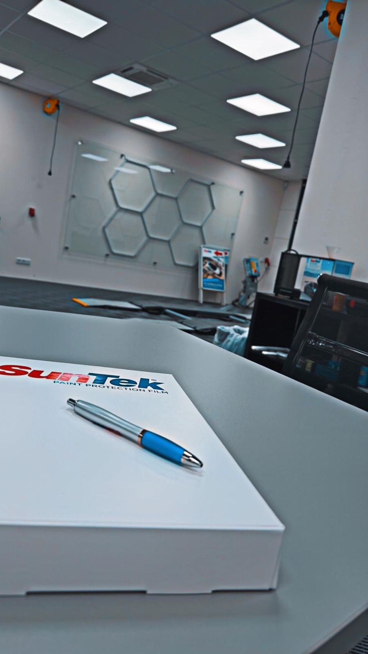 Kugelschreiber auf weißer SunTek Paint Protection Film-Box im modernen Büro mit Wabenmuster an der Wand.