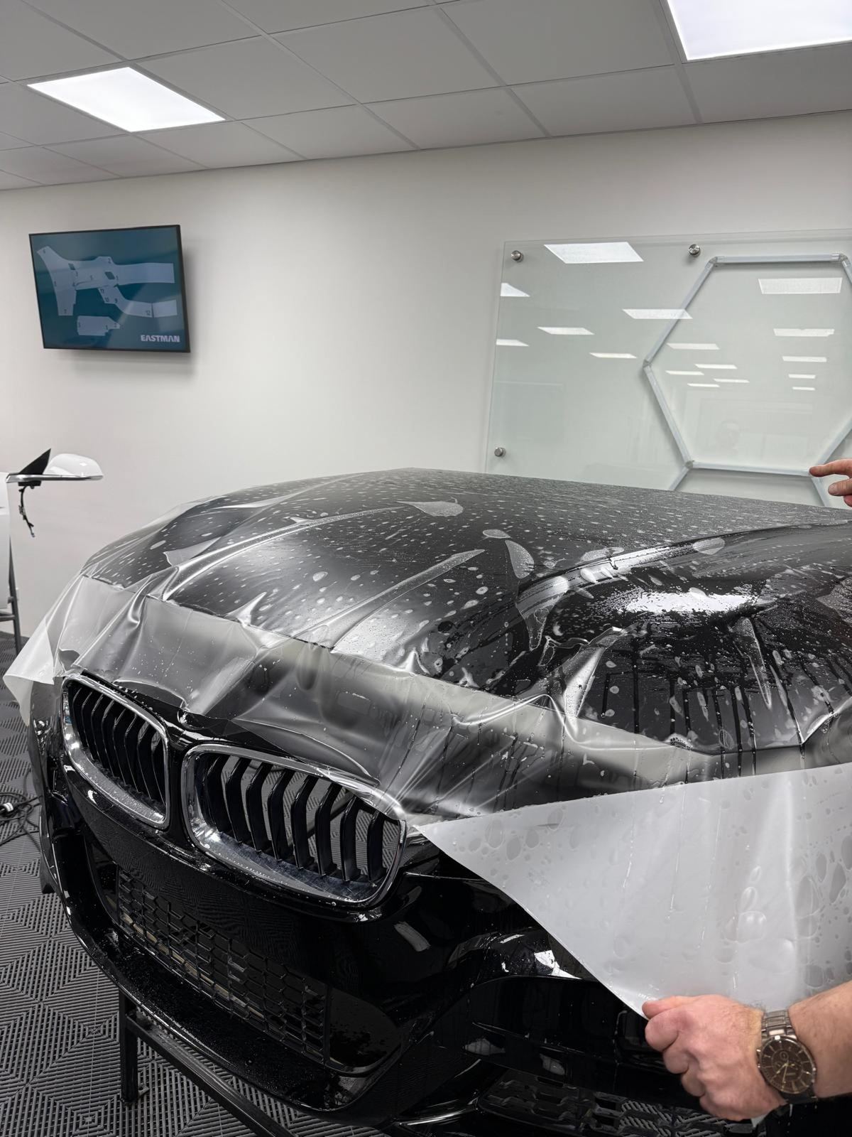 Schwarzes Auto erhält transparente Lackschutzfolie auf der Motorhaube und dem vorderen Stoßfänger.