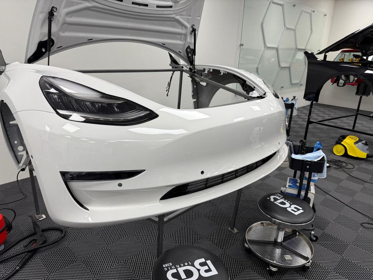 Weiße Tesla Model 3 Frontstoßstange und Motorhaube in einer Werkstatt.