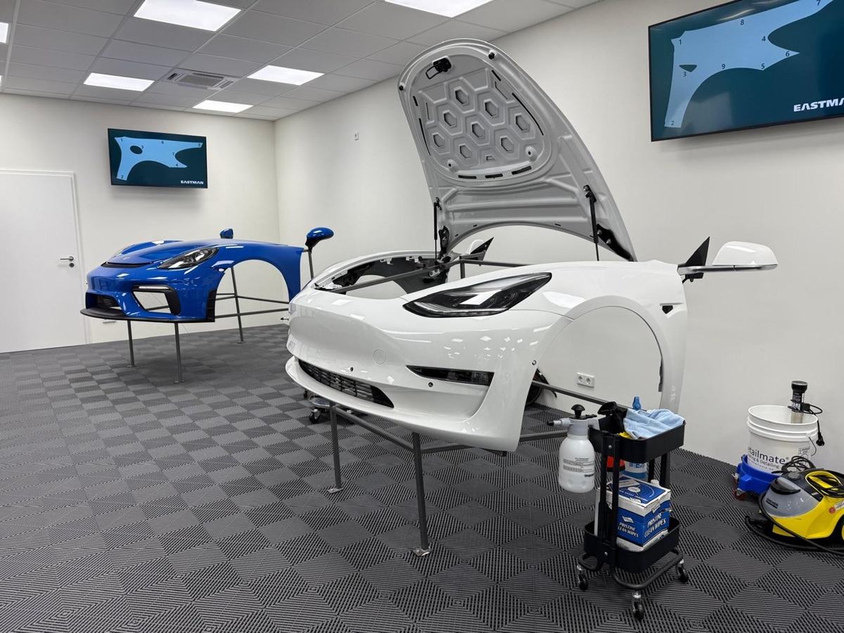 Weißes Tesla Model 3 und blaue Sportwagenkarosserieteile auf Ständern in einer Werkstatt.